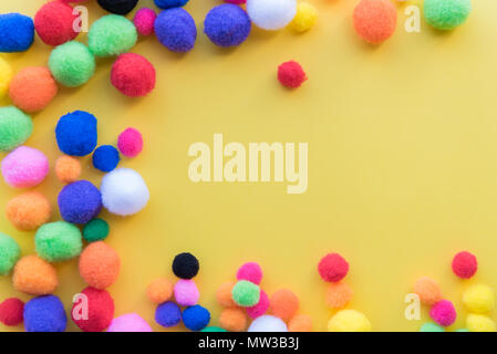 Flat lay arrangement of multi-colored craft pom-poms on solid yellow background with copy space Stock Photo