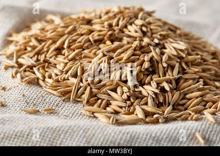 Pile of unpeeled oat grains on homespun tablecloth background, top view, close-up, macro, selective focus. Dietary food. Vegan background. Healthy eat Stock Photo