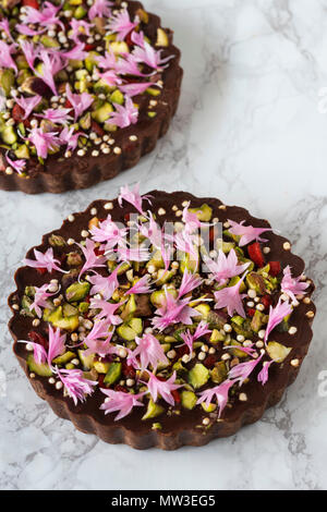 Two raw chocolate tarts decorated with flowers and pistachio on marble Stock Photo