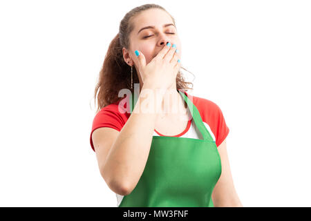 Tired young female supermarket or hypermarket worker yawning and covering mouth as fatigued employee concept isolated on white background Stock Photo