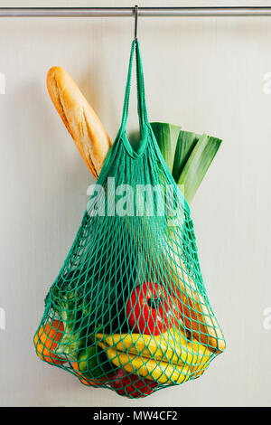 Green string shopping bag with vegetables, fruits and bread hanging on a hook in the kitchen Stock Photo
