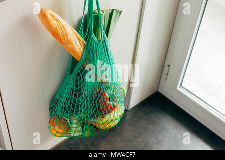 Green string shopping bag with vegetables, fruits and bread hanging on a hook in the kitchen Stock Photo