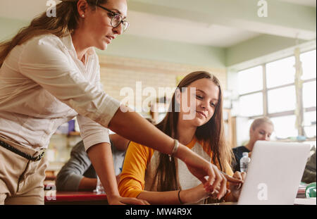 Teacher helping student in classroom. Lecturer pointing at laptop screen and showing something to female student. Stock Photo