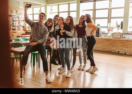 Group of happy young students making a selfie college classroom. Young people in classroom taking selfie with smart phone. Stock Photo