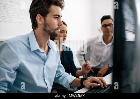 Software developers sitting in front of computer and working in office. Two men and a woman looking at computer and developing applications in office. Stock Photo