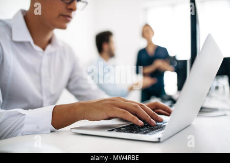 Software developers sitting at office working on computers. Close up of application developer working on a laptop in office with his colleagues in the Stock Photo