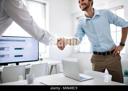 Business colleagues shaking hands in the conference table. Happy businessman greeting colleague in the meeting room. Stock Photo