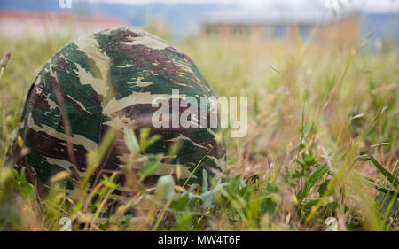 Military camouflage helmet putted down on the ground. Anti-war symbol. Soldier got tired of war. Close up front view, blurred nature background, space Stock Photo