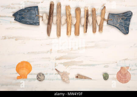 Nautical borders of a decorative hand-crafted fish of stones, pebbles and wood and seashells over textured old white wood with copy space Stock Photo