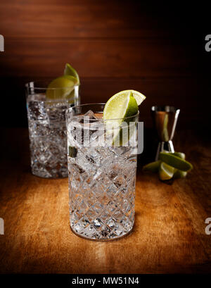 Spotlight on two crystal glasses full of the Gin and tonic cocktail, with a lime garnish, shot on a antique wooden table top. Stock Photo