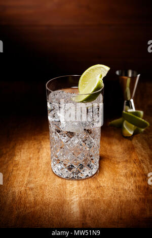 Spotlight on a crystal glasses full of the Gin and tonic cocktail, with a lime garnish, shot on a antique wooden table top. Stock Photo