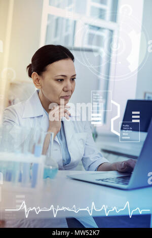Serious woman touching her chin and looking at the screen Stock Photo