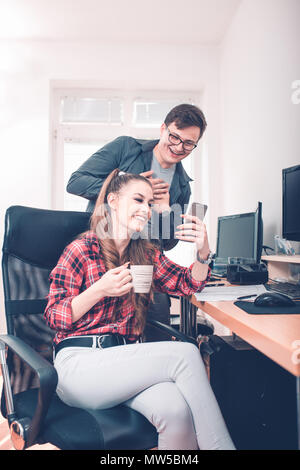 Cheerful coworkers having fun during work break using mobile phone enjoying working together Stock Photo