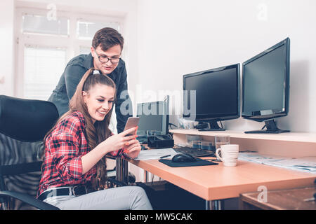 Cheerful coworkers having fun during work break using mobile phone enjoying working togethe Stock Photo