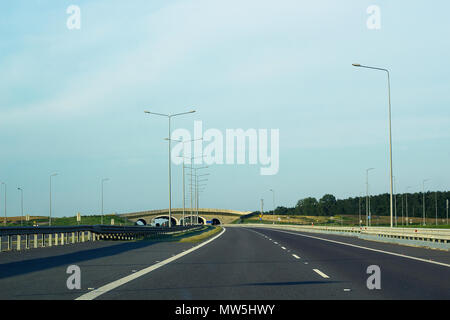 Empty asphalt road, street lights and stone bridge in distance against blue sky Stock Photo