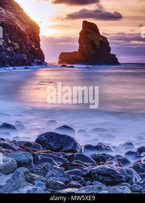 Amazing sunset, Talisker bay on the Isle of Skye in Scotland. Foamy sea, boulders and large cracked rocks with erosion marks. Rocky coastline with sea Stock Photo