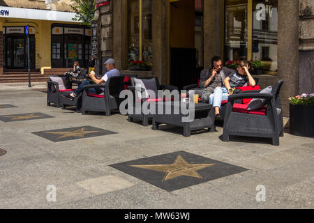 People sitting on chairs outside cafe restaurant in Piotrkowska Street in Łódź, Łódzkie, Poland, showing stars from Łódź Avenue of Fame Stock Photo