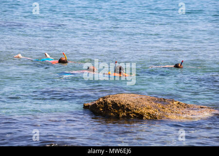 Father and kids snorkeling in the sea near rock. Stock Photo