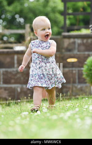 Beautiful Young baby girl toddler at 18 months old with short blonde hair walking in garden - model released Photograph taken by Simon Dack Stock Photo