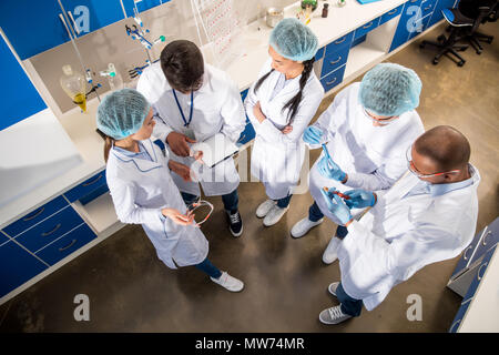 group of concentrated colleagues in white coats discussing work in laboratory Stock Photo