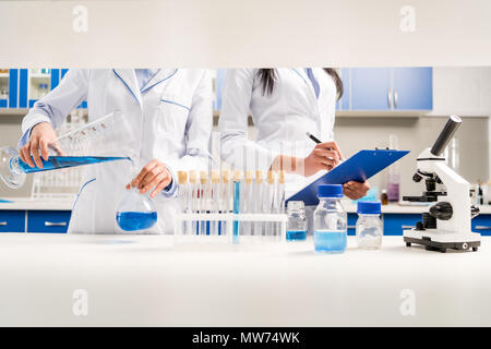 Cropped shot of medical workers working with reagents and taking notes on clipboard in laboratory Stock Photo