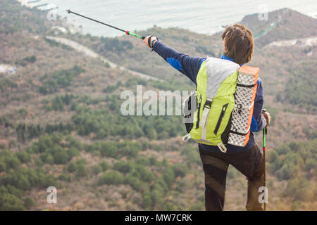 man standing on a cliff in mountains and showing left with pole Stock Photo