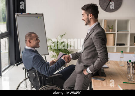 side view of smiling multiethnic businessmen shaking hands at workplace Stock Photo