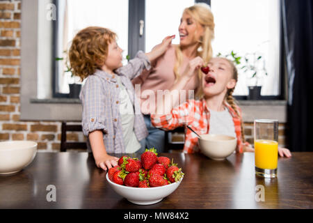 happy young mother with cute children eating strawberries at home Stock Photo