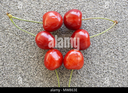 Six fresh red cherries on a grayish background Stock Photo