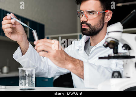 Concentrated male scientist in protective glasses making experiment in chemical lab Stock Photo