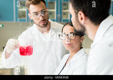 Team of professional young chemists wearing eyeglasses and lab coats making experiment Stock Photo