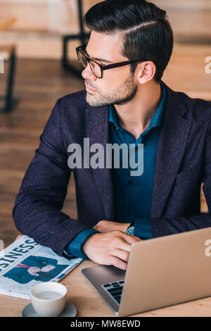 portrait of pensive businessman looking away while sitting at table with laptop in cafe Stock Photo