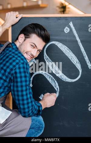 back view of smiling waiter writing 50% sale on chalkboard in cafe Stock Photo