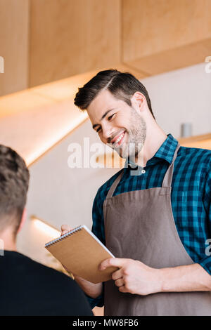 portrait of smiling waiter in apron taking order from client in coffee shop Stock Photo