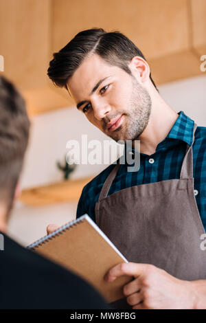 portrait of focused waiter in apron taking order from client in coffee shop Stock Photo