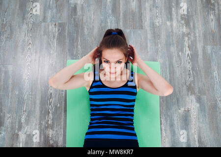 Young beautiful woman  girl wearing fashion sports wear doing exercise on mat  loft gym, top view.  Fitness in gym. Stock Photo