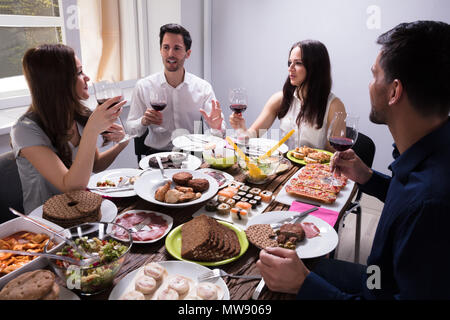Smiling Young Friends Enjoying Food With Glass Of Wine At Restaurant Stock Photo