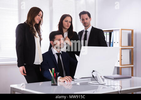 Group Of Young Businesspeople Looking At Computer Screen At Workplace Stock Photo