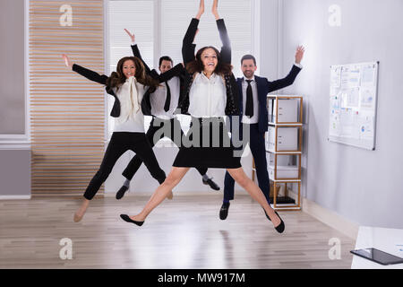Young Businesspeople Jumping In Office Raising Their Arms Stock Photo