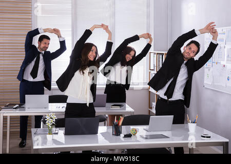 Happy Businesspeople Doing Stretching Exercise Behind Desk At Workplace Stock Photo