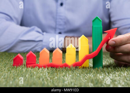A Person's Hand Holding Red Arrow In Front Of Increasing Graph With House Model Stock Photo
