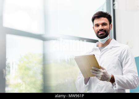 Bearded male scientist in lab coat using digital tablet and smiling at camera Stock Photo