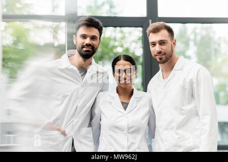 Team of professional scientists in white coats standing together and smiling at camera Stock Photo