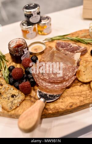 Charcuterie display of salami, cheese, raspberries, grapes, jam, marmelade and crackers on wooden cutting board. Stock Photo