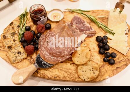 Charcuterie display of salami, cheese, raspberries, grapes, jam, marmelade and crackers on wooden cutting board. Stock Photo