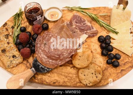 Charcuterie display of salami, cheese, raspberries, grapes, jam, marmelade and crackers on wooden cutting board. Stock Photo