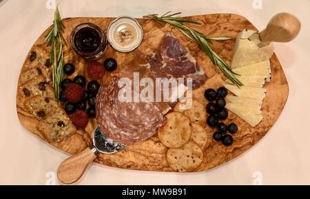 Charcuterie display of salami, cheese, raspberries, grapes, jam, marmelade and crackers on wooden cutting board. Stock Photo