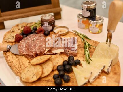 Charcuterie display of salami, cheese, raspberries, grapes, jam, marmelade and crackers on wooden cutting board. Stock Photo