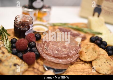 Charcuterie display of salami, cheese, raspberries, grapes, jam, marmelade and crackers on wooden cutting board. Stock Photo