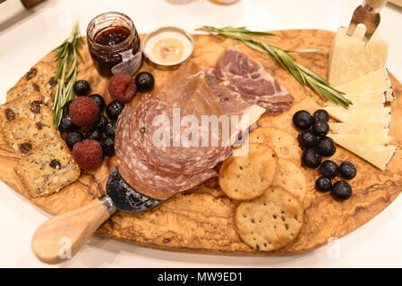 Charcuterie display of salami, cheese, raspberries, grapes, jam, marmelade and crackers on wooden cutting board. Stock Photo